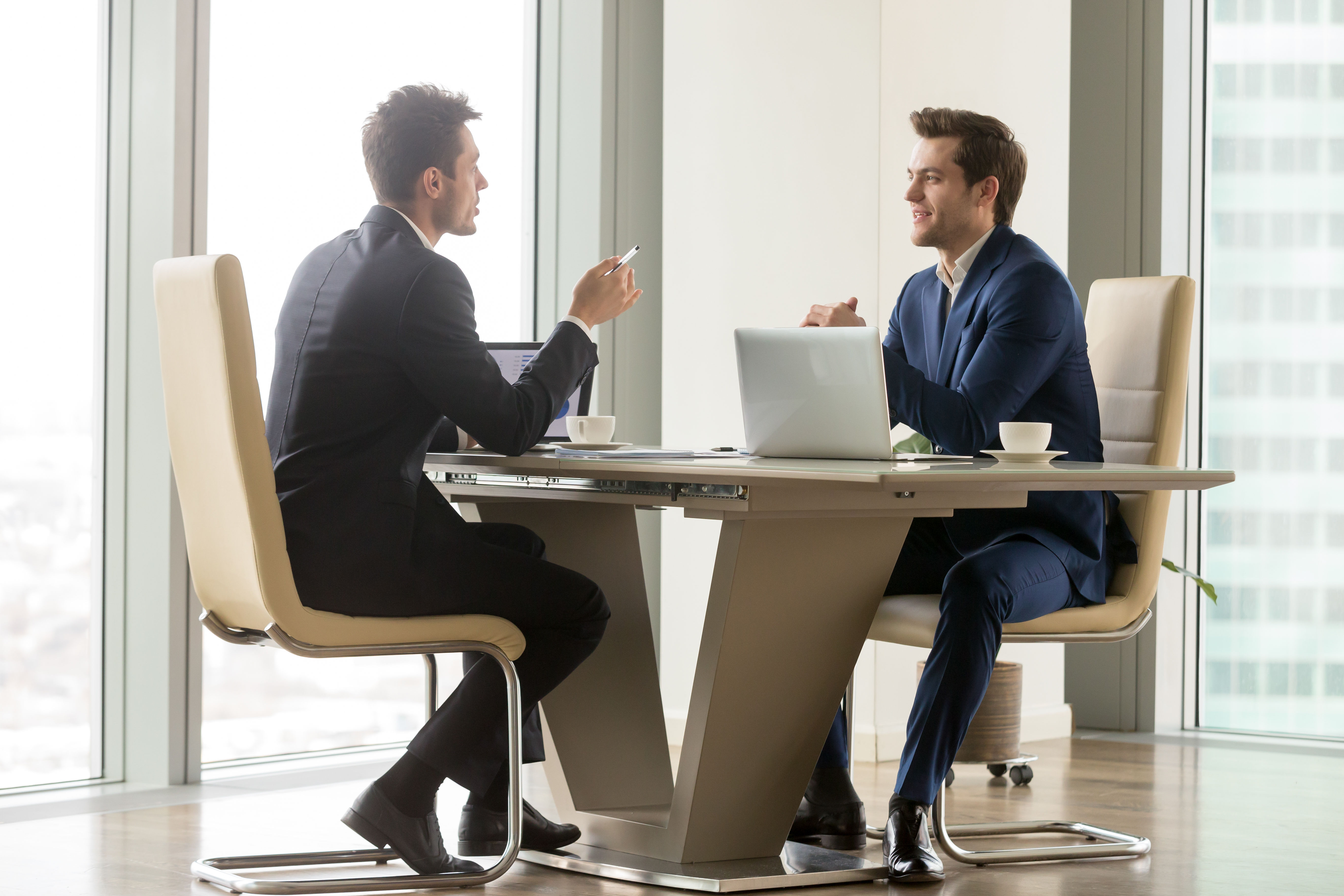  Two business people having a cautious conversation while sitting at a table in an office.